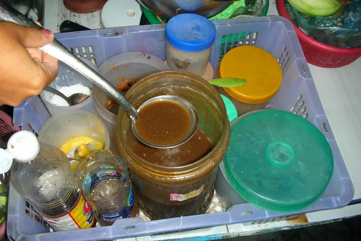 バンコクのソムタム屋台のカートに置かれた容器の中に、プラーラーの魚と褐色の発酵液が入っている。